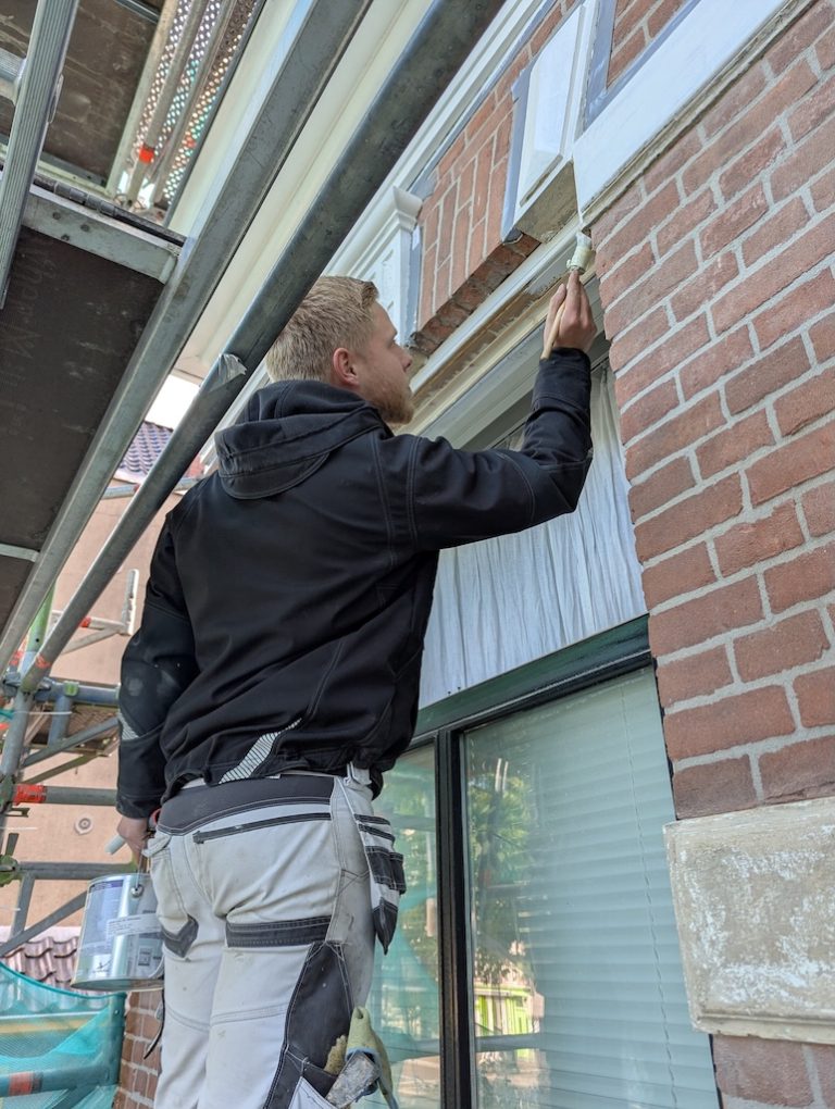 Schilder schuurt het houtwerk boven een winkelpui