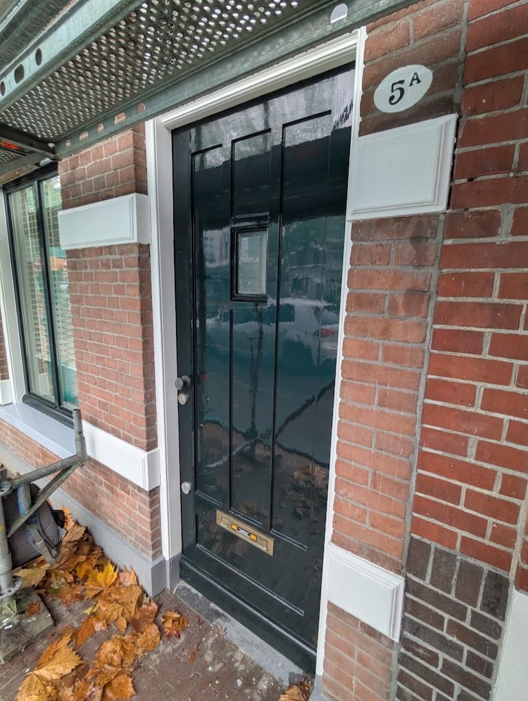Dezelfde voordeur in diepgroen met fris wit kozijn na restauratie
